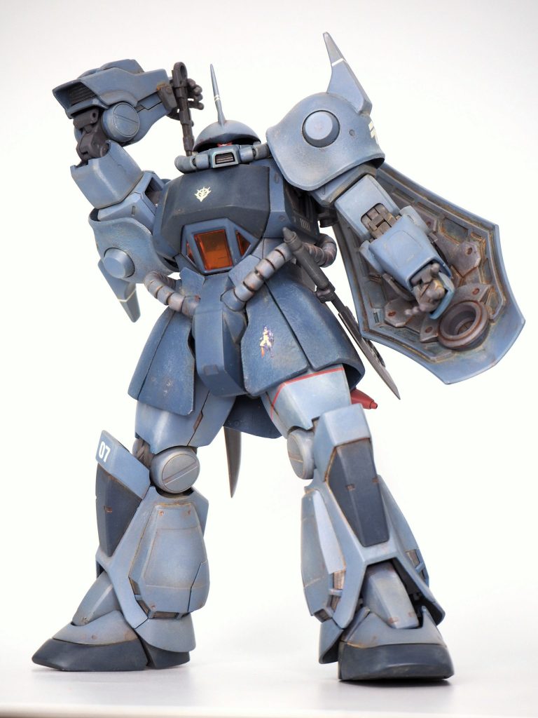 陸戦MSとしての表現としては、まずショルダーアーマーやスカートアーマー等の湾曲した大面積の装甲は鋳造であることをイメージして溶きパテでテクスチャを作り、模型的なメリハリをつけています。次にドイツ戦車のジャーマングレーの退色が青っぽく見えることを参考に、アニメの設定色から著しく乖離しないバランスを見極め、グフの青と認識できる範囲で空気遠近法と塗装の退色を表現しました。 また、錆や埃、バトルダメージはスケール的に大げさにならない程度に留め、やり過ぎないバランスを重視しています。