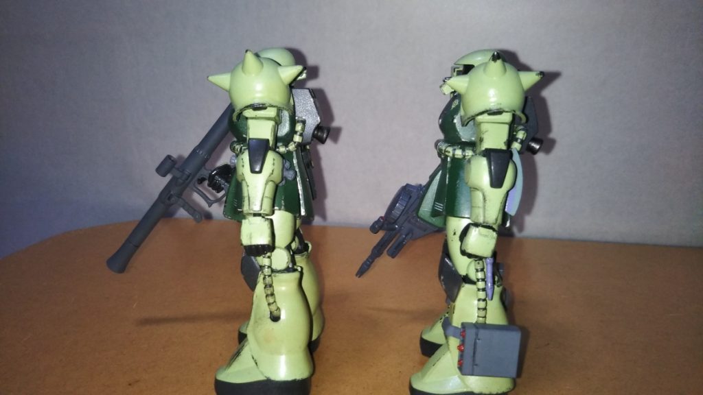 サイドビューです。 機体番号42がブラック曹長機(「第04小隊2番機」の意味)、43がサム伍長機です。 さて、先ほど少し言及したウェザリングの件ですが、この2機、実は微妙にウェザリングのパターンを変えてみました。 具体的には、ブラック曹長は第2次地球降下作戦の時から地上で戦っていた(と言う設定)ので、シールドを中心にあちこちの塗装ハゲを激しめに、しかしバズーカで味方機の支援をするという部隊での役割上、接近戦をする機会はほとんどないはずでは、と考え、ショルダーアーマーのトゲはあまり塗装がはがれていないようなイメージで仕上げました。 サム伍長機はマシンガンとヒートホークを装備しているので、射撃戦のみならず、必要ならそれなりに白兵戦もするはず、と思い、ショルダーアーマーのトゲはタックルで敵を倒したことを表現するように塗装ハゲを入れてみました。 しかしながら、彼の機体はブラック曹長のザクに比べれば新しいモノなので、シールドをはじめ、全身の汚れはそこまでないはず、と考え、若干ですがウェザリングを控えめにしてあります。