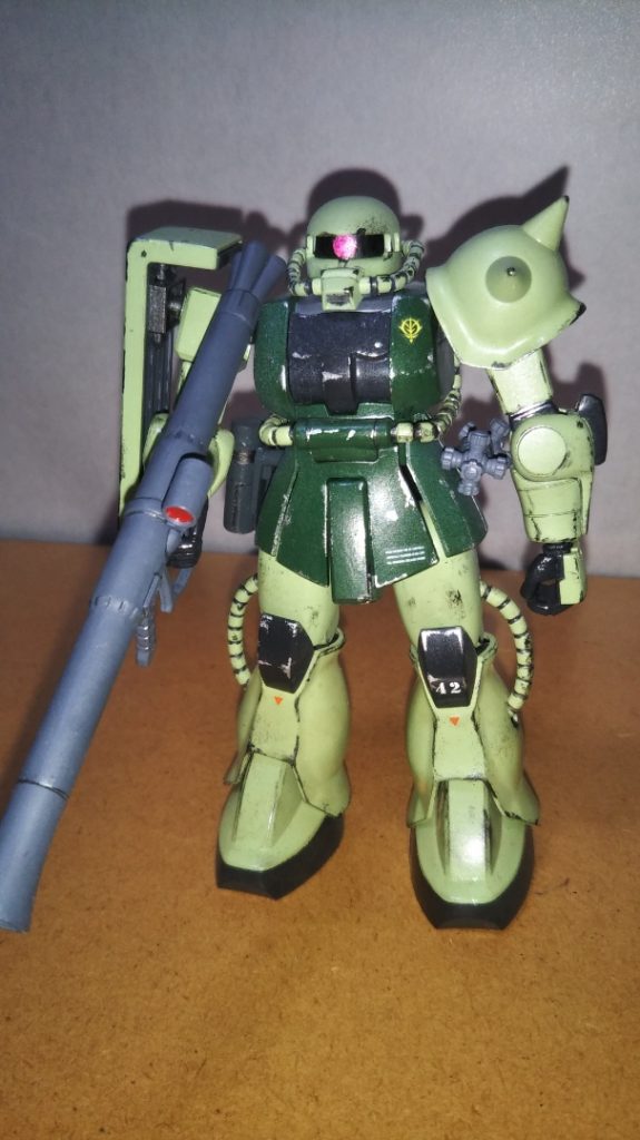 部隊一の射撃の名手、ジョン・ブラック曹長機の正面素立ちです。 こちらのザクはザクとガンダムがセットになった「ガンプラスターターセット」なるキットのモノです。 そういえば説明が遅れましたが、本体は若草色とグリーン、ミッドナイトブルーの3色で塗り分けました(いずれも水性ホビーカラー)。 モノアイは銀色で下地を塗ってから、マッキーのピンクで塗装しました。 さらに関節などの細かな部分を塗り分けたあと、デカールやシールでマーキングをし、足元を中心に黄土色のパステルをけずった粉を平筆ではたき、つや消しトップコートを吹いてあります。 いつも通り鉛筆やシャープペンでスミ入れをしたあと、仕上げに銀色と黒鉄色でウェザリングも施しました(ウェザリングに関してはかなりこだわった部分なので、後ほど詳しく解説します)。