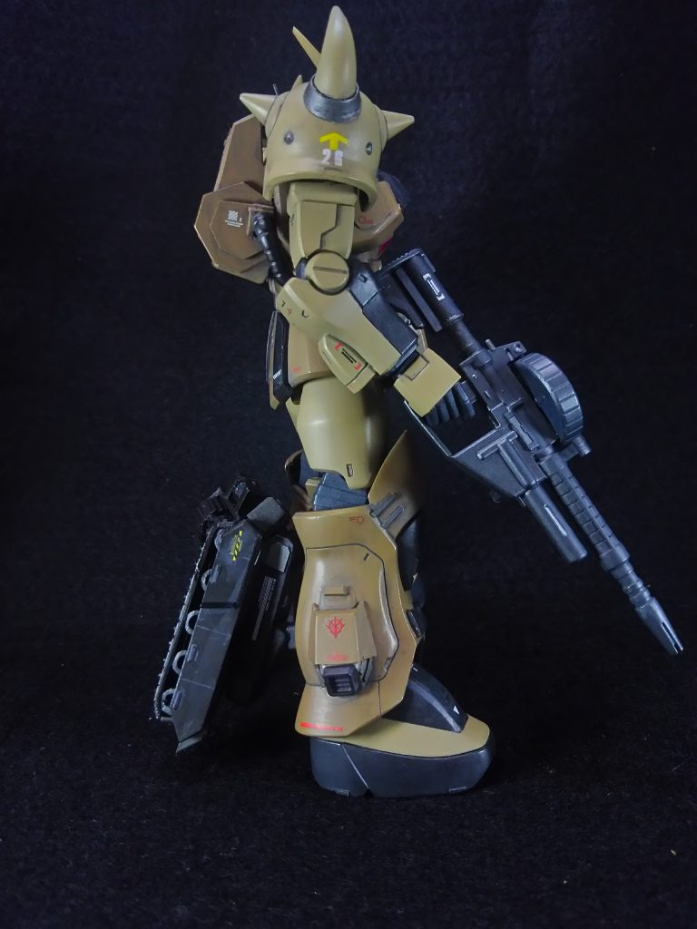 北アフリカ 待つ事、数十分。 デザート・グフの振動センサーに反応が有った。モニターに赤いマーカーが2つ表示される。 「第13地上機動歩兵師団だったか?良い仕事をする」 2つのマーカーは真っ直ぐこちらへと近付く。残り約1㎞、500m、100m・・・。 マーカーがほぼ真上に来た時グライムは攻撃を仕掛けた。 突然盛り上がる地面、その砂の中から飛び出した何かが目の前のGMの持つビームスプレーガンを叩き落した。 驚くGMのパイロット、見ればMSの右手が切断されている。更にもう一度伸びてきたそれが左腕に巻きついた。 「ヒートロッドか!?」 機体を下げ、引き千切ろうともがくGM。 「改良されたヒートロッドは優秀だな!」 グライムはヒートロッドに電流を流して、動きを止め、左腕に装備されたヒートサーベルを1段階展開して切り裂いた。 「グフか!?」 もう1機のGMが爆発して巻き上がった砂目掛けて銃を撃ちながら後ろへとジャンプした。 手応えを感じず苛立ちが跳ね上がる。 敵部隊から逃げた先に得体の知らないMSと遭遇して最後の僚機がやられたのだ。 「くそったれが!」 叫んだ時、爆発の左側から砂煙を上げて砂漠迷彩のグフが滑り出て来た。     まるでスケートでも吐いてる様に、足を揃えたまま砂上を滑るグフ。 GMの着地を狙ってマシンガンを放つ! シールドで防ぐが機動力が違いすぎた。 一気に距離を詰めたグフが目の前に迫る、ヘッドバルカンとビームスプレーガンで応戦するがまるで当たらない。 「機動力が違う!」 右へ左へと交わしながら迫るグフ擦れ違い様にヒートサーベルを薙ぎ払ったがこれはギリギリ躱した。 「な!?」 なんとか回避したが喜ぶ暇は一瞬も無かった。GMの腕にヒートロッドが巻き付いていたのだ。 「これで終わりだ!」 ヒートロッドを引いてGMの体勢が崩れた所にヒートサーベルで斬り掛かる! 「くそ!」 GMのパイロットは機体を捻って紙一重で回避した。 (躱した!)と思った刹那、機体に衝撃が走りGMの胴体は逆袈裟で斬られていた。 グライムはヒートサーベルをもう一段階伸ばしVの字を書く様に振り下ろした剣を斬り上げたのだ。 巻き付けていたヒートロッドを解いて、後方に大きくジャンプして距離を取った所でGMは大爆発を起こした。 「やりましたね、少尉!」 「お見事です」 グフから遅れて砂中から出て来て周囲を警戒していた2機のデザート・ザクが近寄って賛辞を送る。 「ありがとう。これでこいつの量産も近いな」 「自分にも配備されるのが楽しみです」 「その時迄に乗り心地が改善されるのを祈ってますよ」 「そこはしっかり上に伝えておくさ」   無事生き残り、テストも終了した3人は、GMを追い立てた『第13地上機動歩兵師団』と合流後、帰路に着いた。 この後、デザート・グフの開発凍結を聞いたグライムはそのままアフリカ戦線に残り、受領したグフ・デザートで多くの戦果を上げ無事1年戦争を生き抜いたのだった。