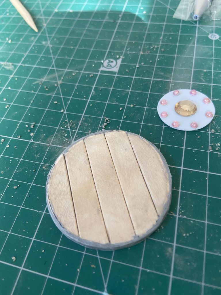 ラウンドシールドはアイスの棒を円状にカットしらプラ板とパテで整えて作成。右上の物を金具にしようとしましたが、やめました。