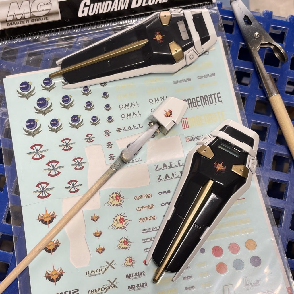肩とシールドに発売当時に購入したガンダムデカール18のオーブマークを貼りました。 発売から15年くらい経っているものなので、白が黄変してもろくなっていました。 台紙から浮かせて貼る際に2枚 まっ二つになり、1枚は使用不能に(>_<) 台紙から浮く前の状態でスライドさせて貼った方が、傷んだデカールへの 負担は少ないようです。