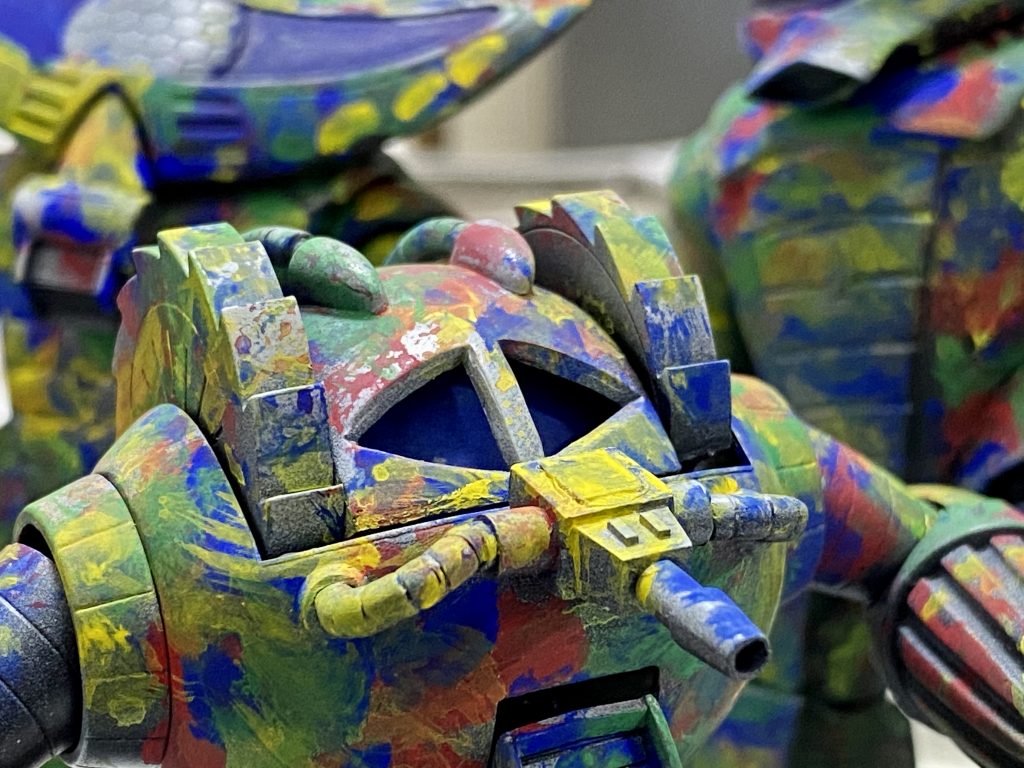 ●塗装についてスミマセン、塗装中の写真をちゃんと撮っていなくてこんなのしかないのですが(笑)、右奥にアッガイがいます。グレーサフを全体に吹いてから、アクリルガッシュでレインボー下地をつくります。どういったパターンがいいのかまだ試行錯誤中なんですが、今回は割と大きめの筆で大まかにしてみました。小さいパターンにすると仕上がりが均一になるようで、このあたりはキットのスケールによって使い分けるのがいいのかな、と思います。色は赤、青、黄、緑の4色を使いました。下地ができたら、茶色を重ねていきます。塗膜が厚くなるとせっかくの下地が消えてしまうので、様子を見ながら薄く伸ばしていくように塗ります。塗り重ねて2,3回目くらいで発色してくるくらいがいいと思います。