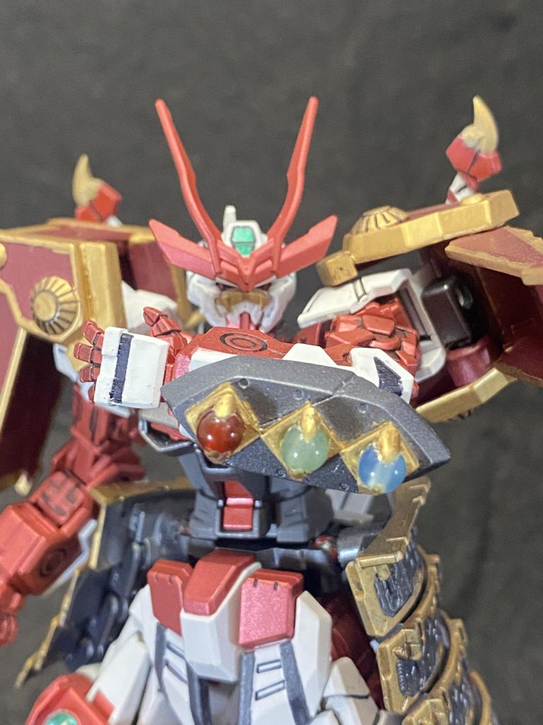 ここからは説明と一緒に制作しながら考えた設定という名の妄想も垂れ流していきたいと思います。読まなくてもいいです。ダイバー名：桃我(トウガ)機体名：桃王　亜須斗零　頑駄無おとぎ話のキャラをモチーフにしたガンプラのみが加入できるフォース「フェアリーテイル」に所属しているダイバー。少し暑苦しいのが玉にキズだが、気さくでおおらかな性格。アバターは桃太郎を意識した姿をしており、語尾にも「ござる」を付けて話す。普段から「犬」、「猿」、「雉」のペットを連れている。このペットは特別なミッションで手に入れたもので、プレイヤーと会話することが可能。しかし、3匹ともかなり個性的な性格なのでトウガとその3匹との漫才じみた会話が仲間内で面白がられている。戦闘では基本前衛。正々堂々を信条とし、常に全力でぶつかれる相手を求めている。その昔、共に研鑽を積んだ仲間がブレイクデカールを使用したマスダイバーにむごたらしく倒されたことでトラウマを負いGBNを去ったことがあり、その一件からブレイクデカール含む、全ての不正行為を行うダイバーを憎むようになる。相手が不正行為を行っていると判明すると態度が一変、今までの明るい表情から冷酷な表情に変わり、戦い方も手段を選ばないなんでもありの戦法に代わる。あらゆる手を使い相手を追い詰め、無慈悲に、徹底的に破壊するその姿から「桃太郎の皮をかぶった鬼」と陰で呼ばれている。「気尾玉(キビダマ)」左腕の手甲にはめられている3つの宝玉。それぞれの宝玉に3体の御供が封じられている。モンスターを呼び出すということでモンス〇－ボールと家来にするために与えるキビ団子から着想を得て作りました。余ってたバルバトスの腕パーツに、プラ板とビーズを使って作ってます。色的にキビ団子というより3色団子みたいですね。