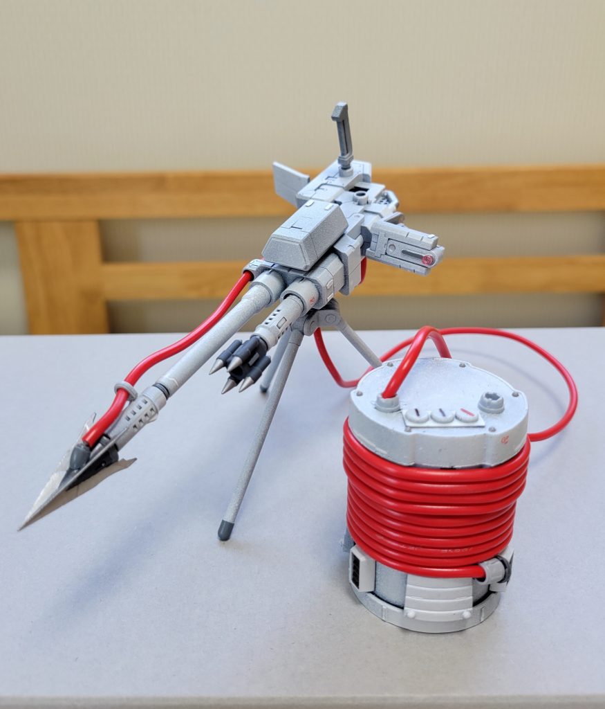 敵兵器捕獲用の武器です。発想元がミシンなので、武器も針とか糸っぽいのを使う感じで考えました。この武器の使用方法は、赤いケーブルの付いた銛(針ではなくモリ)を、相手兵器へ発射・突き刺します。赤いケーブルはビームサーベルでもすぐには焼き切れない特殊ケーブル。突き刺して繋がった相手は逃さず、最終的に捕獲を目標としています。某ミシンメーカーが地球連邦軍に売り込むため作成した、敵兵器捕獲用武器と、RX-78のデータを基に作成した捕獲専用MSからなるパッケージです。