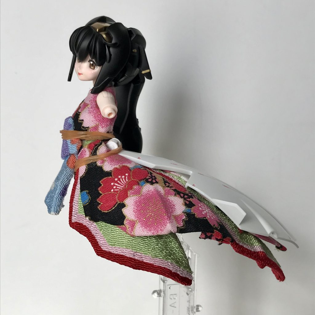 スカートの造形もそのままで、布を貼り付けただけです。後ろ側の外側スカートは成形色のまま何もしていません。十二単では裳(も)と呼ばれる布を腰から垂らすので、ちょうど良い感じです。ちなみに、布で厚みが増したり、接続部がふさがったりするので、そのままではスカート等と胴体を結合できなくなったり、確実にははまらなくなりました。無計画にやってますので…(汗) というわけで、ボンドGPクリヤーで無理やり接着してあります。写真はその固定のために輪ゴムを巻いてあります。