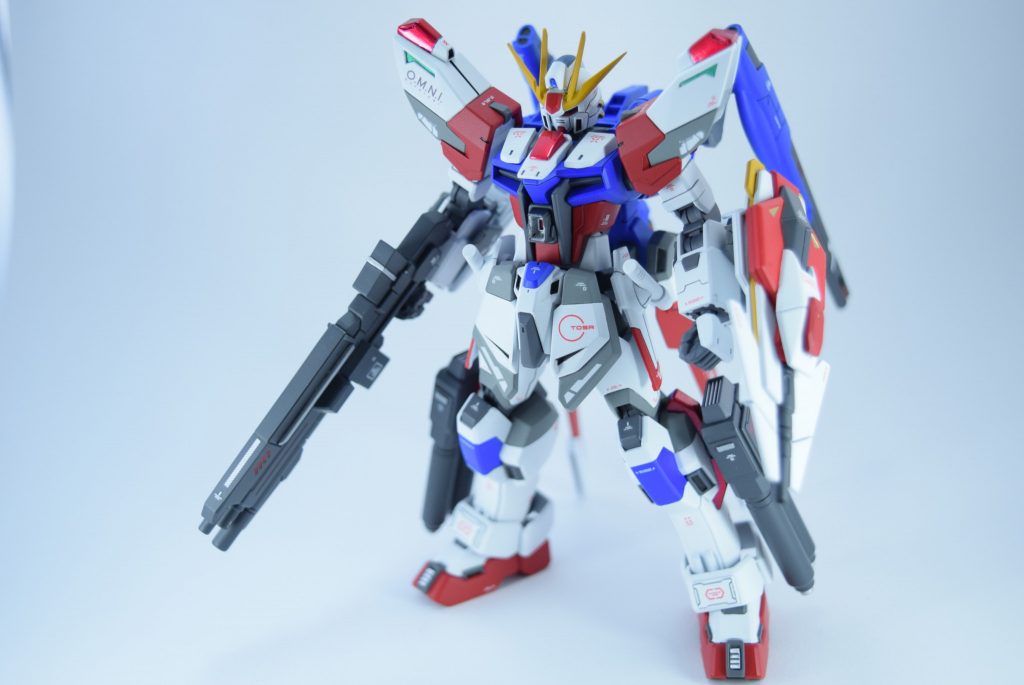 自分だったらスタービルドストライクをこう強化する、というコンセプトで作成しました。機動力を維持したまま、火力、防御の強化を図っています。バックパック、腹部、下腿は高出力のビーム砲ですが、偏りを補うためライフルは実弾。3つの砲身から、2種の弾薬とグレネードが使用できるようになっています。各部に少しずつ装甲も追加しています。