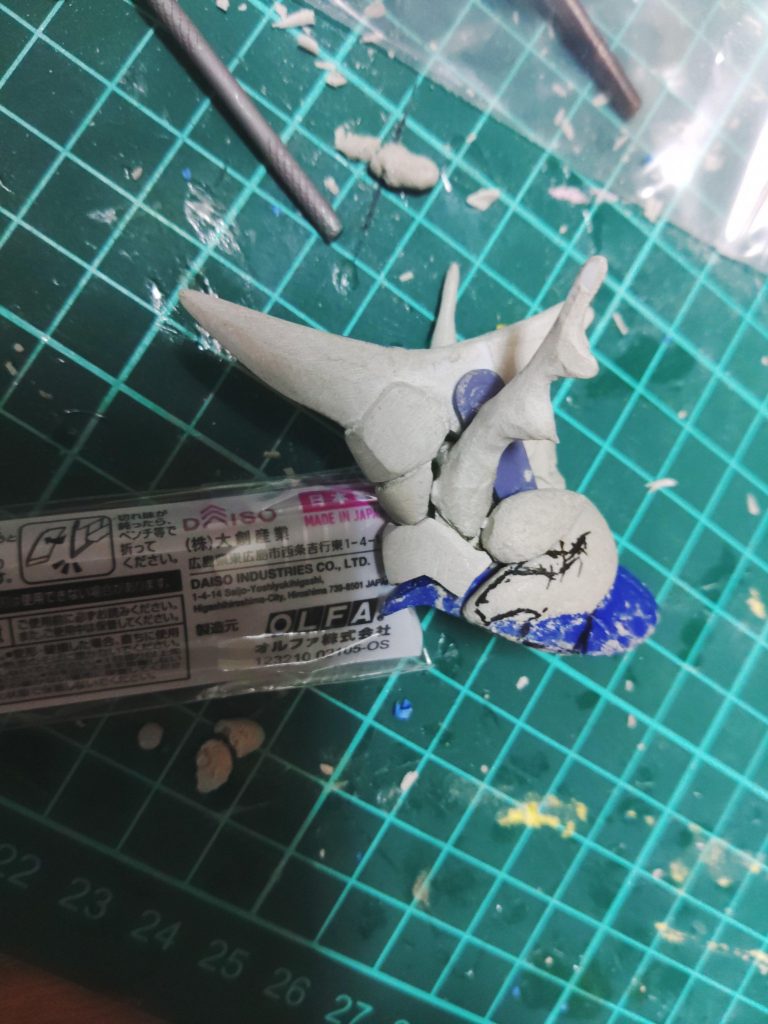 稼動部の配置,パテを盛る位置等が決まったら、大体の形をプラバンで作って、それを芯にパテを盛って削って盛って削ってCut&Try。モノアイ上部の額当てのような部分は、塗装後にモノアイ等を仕込むため間にマスキングテープを挟み取り外せる様にして成形。下向きの角(銀色の角)は、折れてしまうので中に0.8mmの真鍮線入れました。