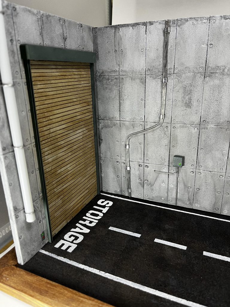 シャッターの枠はプラ棒とプラ板で作成。ジオラマのくせにちゃんとサフ吹いたり、エアブラシで塗装したりしました。シャッター横にはシャッター開閉用のスイッチも配置。電線的なものの横には配電盤みたいなものも配置しました。はんだ線は曲げやすくて助かります。