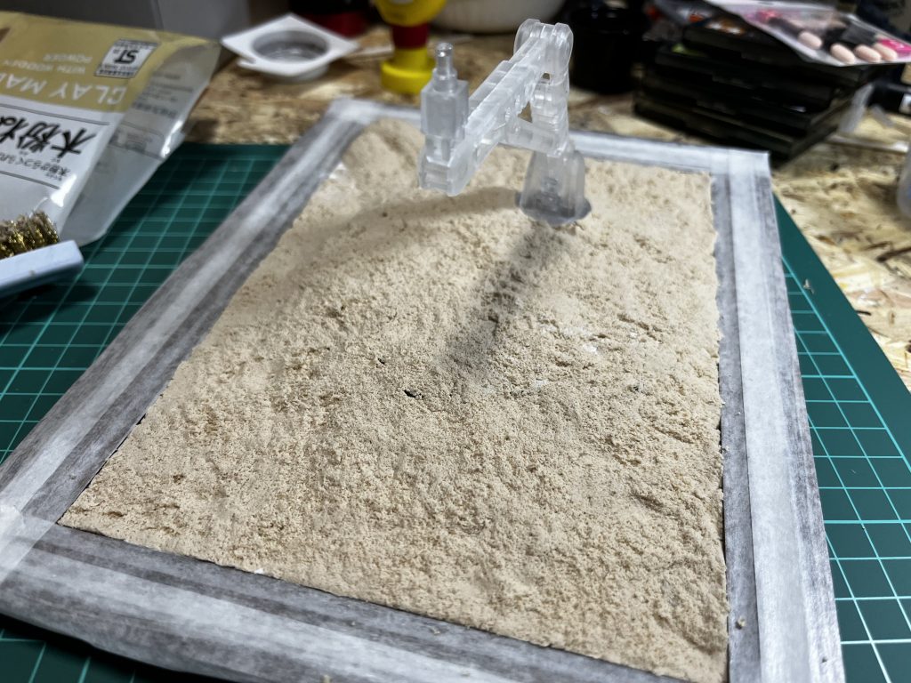 ジオラマの初期工程です。ダイソーの写真たてにアクションベースを貼り付けて上から木粉粘土をのせました。そのあと金属製の歯ブラシみたいのでトントンして地面の感じを出しました。まぁ、ほとんど土煙で隠れるんですけどね。
