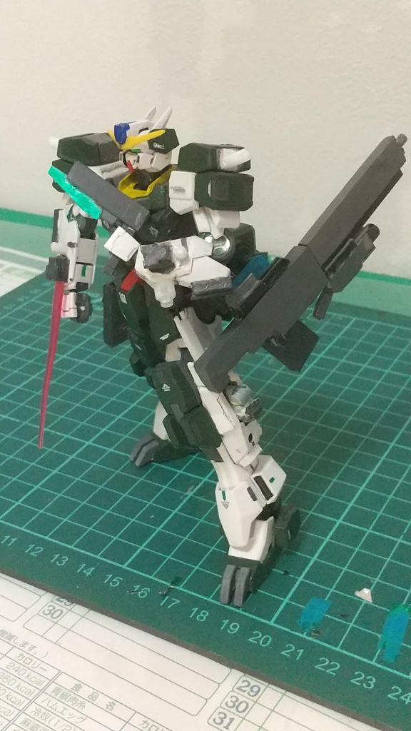 GNピストル改はケルディムガンダムのGNピストルIIの刃を新素材のパーツに変更し後はそのままの設定、本当はケルディムのピストルIIをそのまま使いたかったのですが後のギミックで問題が起きたため新しく自作、ホルスターもサーガのやつだと取りにくいため新しく作りました。腰辺りにあるためすぐに取り出して速打ちができる。あとGNスナイパーライフルも不使用時にはホルスターにマウントできるようにしました。腕のGNバルカン(GNソード)は固定型のビーム兵器本当は頭部に付けたかったのですが頭部にはカメラがあるため腕に設置、ミサイル等の迎撃に使用、     GNビームサーベルとしても使え狙撃中に他の敵に接近された時に武器の持ち替えをしなくてもすぐに反撃することを目的に使用足の本当はカメラがあるところですがそこをカメラの機能を無くし武器の格納庫にしました。まず上の部分にはビームサーベルを付けました。理由として近接戦も想定すると腕の固定用ビームサーベル(ガン)だと手首の可動を使えず対応の幅が小さくなることやいくらGNピストルに刃があるからといって威力も関節に当たればいけるかもしれないけど1~2発だけだと装甲貫通しないため使いやすく威力もあるGNビームサーベルを採用しました。場所も手がすぐに届きやすい太股辺りにしてサーベルを抜きやすい位置にしています。あとサーベルの柄の部分が凹になっていて2つのビームサーベルを合わせるとインフィニットジャスティスみたいに両刃にもできます。正直両刃の実用性はあまりないと思いますが別に付けても大きさとかに変化ないしあった方が何かに使えるかもと軽い理由でこの形にしましたその下の元カメラがあった位置には雑に投げて強い手榴弾、逃げ隠れ時に煙幕、相手の攻撃が激しい時用の粒子撹乱幕の3種からミッション毎に選び片方3個まで収納でき最大6個まで持てるようにしました。理由として後の紹介するビットにカメラ付けた方が見える角度や自由さが増えていいじゃんあとユーラヴェンガンダムみたいに身を隠しながらビットで見るもできるという理由でここは手榴弾系にしました 。その下には3mm穴を開けてミサイル等の追加装備ができるようにして拡張性が持てるようにしました。さらにその下のスペース部分と後ろの脹ら脛にはここからは見えませんが可動域は邪魔しない程度にバーニアを付けてより機動性を高めました。