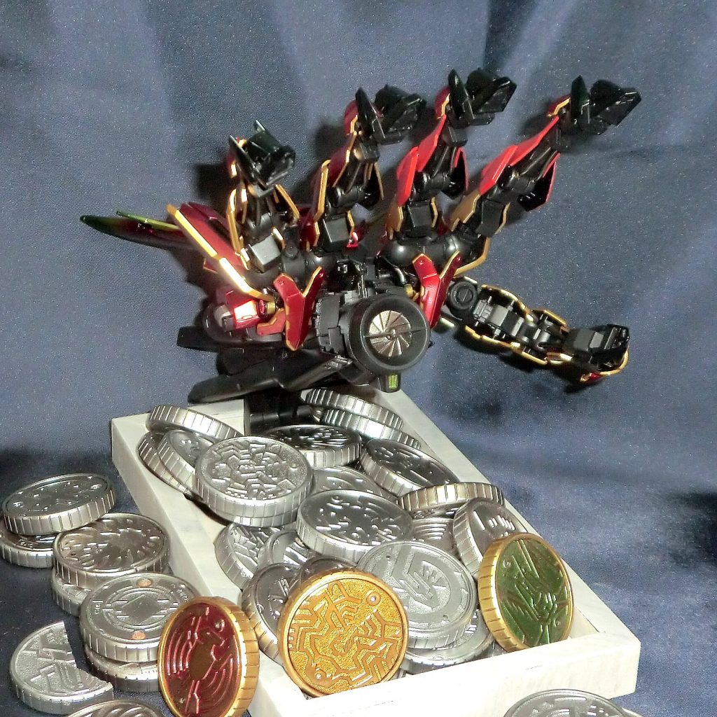 ガンダム設定としてはモビルアーマー:アンク厄祭戦時のモビルアーマーの1機で、本体部分さえ残っていれば撃破したモビルスーツのパーツを自機の一部にしてしまう拳を思わせるそのシルエット中央部から発せられるビームは円盤の形状をしているオーズでの「命」という意味ともとれるちょうどいい設定