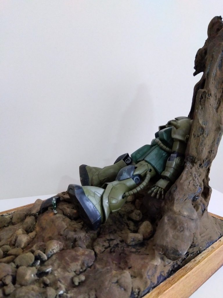 地面は紙粘土と木粉粘土、その上からクラッシャブルストーンを散りばめました。ザクが寄りかかる部分は既存のジオラマを流用。水性絵の具の黒で全体を塗った後、情景用テクスチャを塗り込みました。