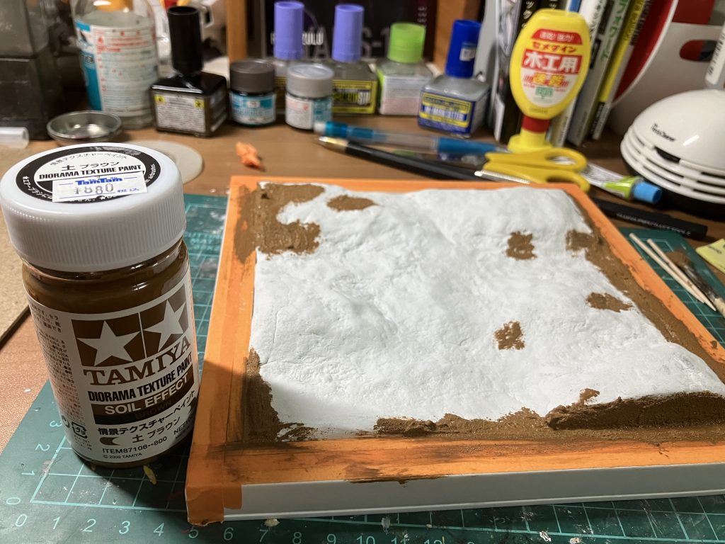 台座の作成。ダイソーのフォトフレームの裏をプラ板で接着→内側にスチレンフォームを接着し形付け→紙粘土を上から重ね、岩石感を出すために丸めたアルミホイルを押し当て跡をつける→乾燥して割れた部分にタミヤのテクスチャーペイントをもりつけリカバリー