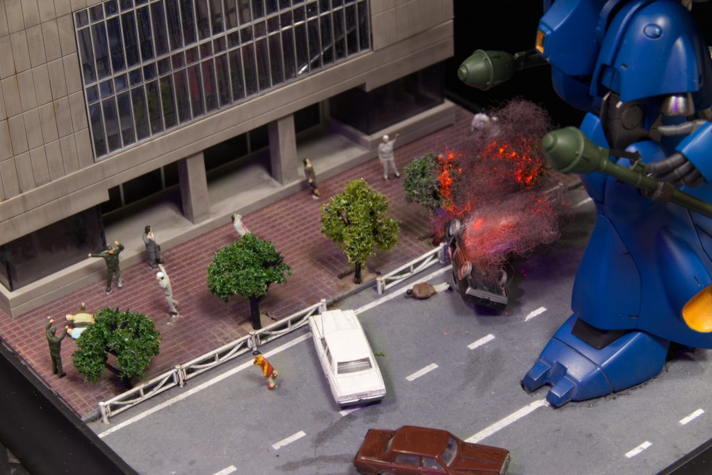 道路は塗装し、白線もマスキングで塗ってます。適宜ウェザリングして使用感も出したつもりです。人々はケンプファーを見上げるまたは、走って逃げるというような想定。手前の車は慌ててハンドルを切って、ガードレールというかポールに激突、炎上しているという場面にしてみました。緊迫した場面らしくなったと思います。