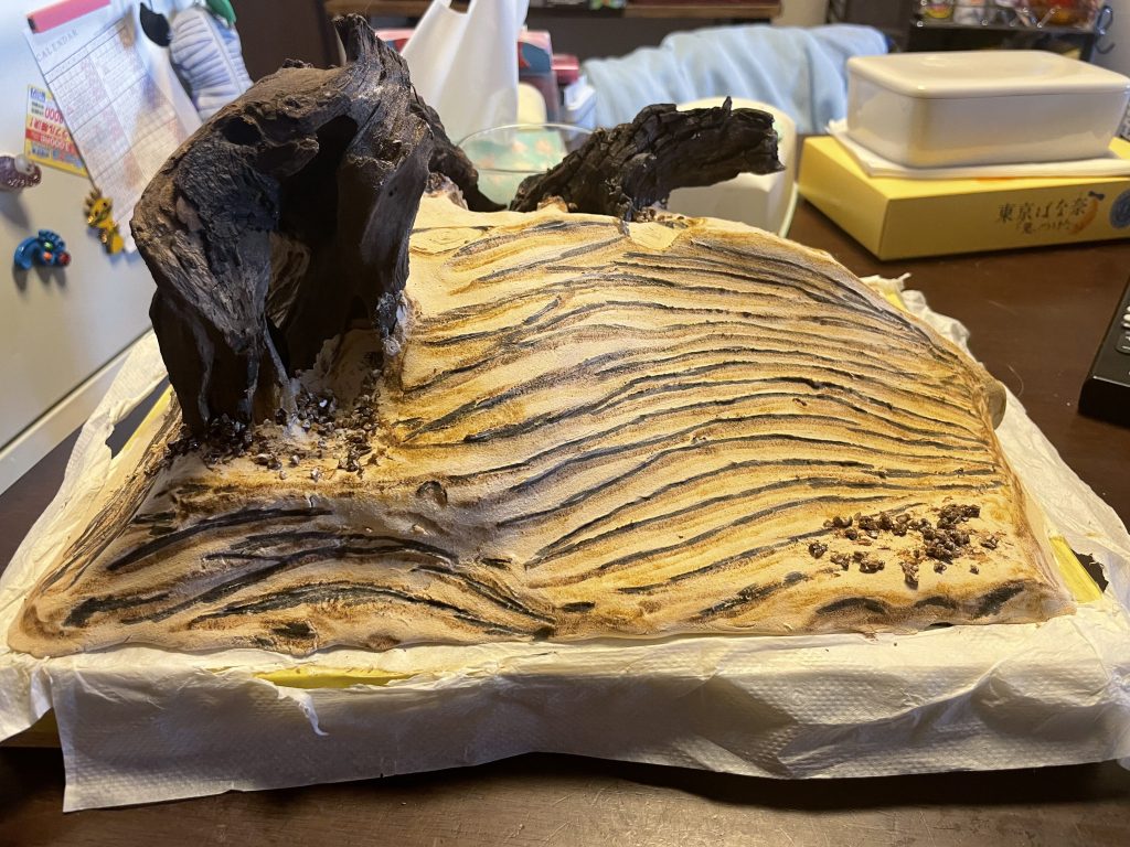 木粉粘土で砂漠を作り岩に見立てた流木を配置した状態。指と爪で付けた風紋を立たせる為に下地の色を入れています。