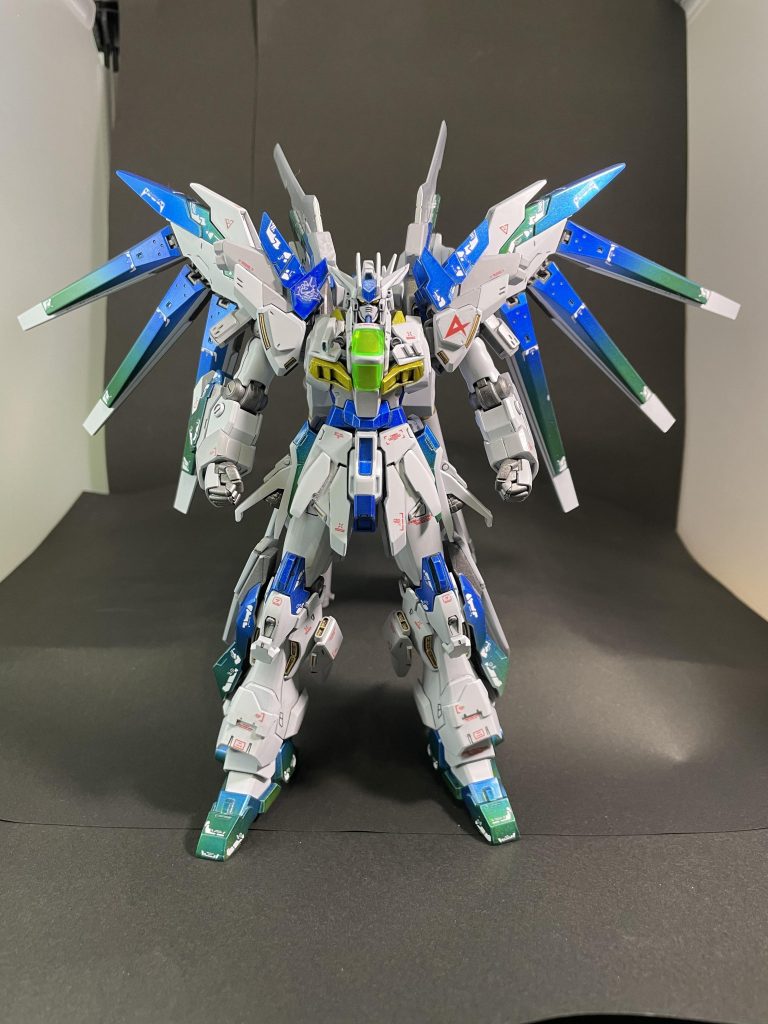 まずは正面素立ち。素体をシナンジュスタイン、外装や武器•シールドをHi-νガンダムブレイヴ、ユニコーン、ガンダムダブルエックス他ジャンクパーツを使用。デカールは市販の水転写デカールを使用。以下オラ設定アクシズ落下を阻止し、帰還したアムロのために、シャアの反乱、ラプラス事変、不死鳥狩りを経て得られたνガンダム、シナンジュスタイン・ユニコーンガンダムの技術を統括・再構成し、ニュータイプ(と言うよりもほぼアムロ)専用のオールラウンド対応型MSとして開発された。いわゆるHi-νガンダムのif機体。機体ベースをシナンジュスタインとしつつも、νガンダムの強化発展案として装甲や武装を配置、サイコフレームも導入されており、パイロット適性に応じて機体性能も向上する。本来機体装甲は青一色のはずであったが、一部はサイコフレームの共振により緑がかったグラデーションになっている。各ベース機体よりマッシブなシルエットであるのは、後述のロングレンジライフルや、ブースターの荷重に耐えうるよう各部を補強した結果である。しかしながら、この補強はあくまで機体本位のものであり、パイロットへの負荷は考慮されていない。武装はサイコミュ兵器のフィンファンネルに加え、バックパックブースターに取り付けられた2本の実体剣「ファンネルブレード」もサイコミュによる遠隔操作が可能。また、このブレードは長距離ライフル「インサイザー」に装着することで高出力砲撃のブレを修正するバランサーの役割も果たす。砲撃の際は形状と構え方から弓矢を連想させる(ことを意図した)ことから、メカニックからは「アーチャー」「ロビンフッド」などと呼ばれている。コードネームは「ナイトヘロン(五位鷺)」。ナイチンゲールへの対抗意識から命名されているが、正式決定まで別候補「ロビン(駒鳥)」の名称と接戦を繰り広げていた。…という脳内設定。考えながら作るとモチベーションも上がって楽しいです。
