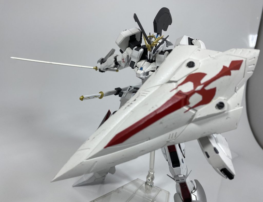 [大型盾　ベイル]本機の左腕に装備される大型のカイトシールド。手首で保持しているわけではなく、膝あたりから伸びるサブアームにより懸架されており、この大型盾を使用していても、左腕そのものは自由に動かすことができる。