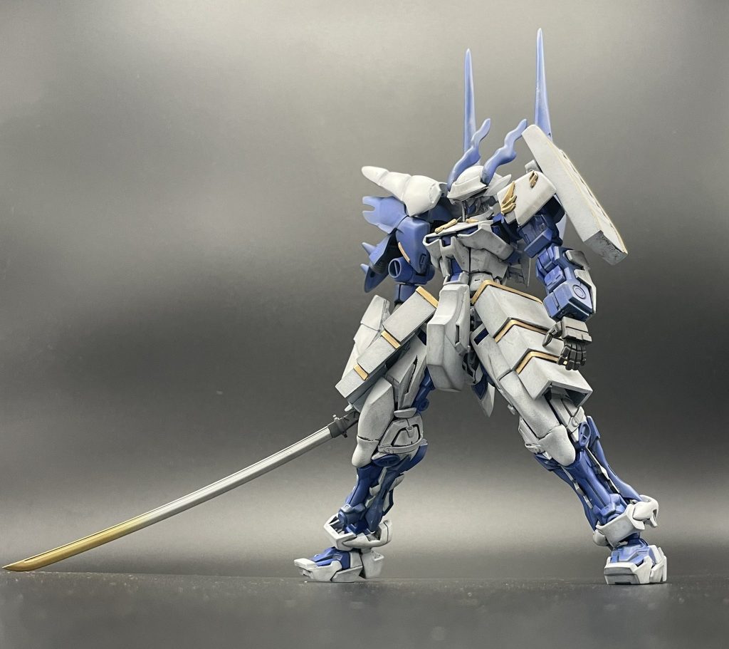 HGのお腹パーツにRGの下半身の接続にはRG側に3ミリランナーを使用。そのままでは短く感じたのとMSジョイントとの接着強度に不安を感じたのでプラ版で1ミリ延長しました。頭部はベースの機装兵ノヴレスにトライバーニングのエフェクトパーツを加工したものを使用。胴体はゴールドフレームをベースにMSエンブレムのネオジオンマークを切断し、接着。右腕はシナンジュの肩に、ジンハイマニューバの足追加パーツにパテで形状変更。肩より下は、もとのゴールドフレームの肩内部パーツにMSGのマイナスモールドを貼り付けたものを移植し延長しています。二の腕より下もゴールドフレームをベースとし、右腕追加装甲をプラ版で自作。接続にはボールジョイントを使用してます。それにあわせて上腕もパテで装飾。手首はサンドロックのものを使用し、刀はMSGの日本刀を手首にハマるよう持ち手を削り込んでいます。左肩はゴールドフレームのものにMSエンブレムを貼り付けて装飾。追加装甲はHGザクⅠについてくるシールドをベースに0.4ミリくらいのプラ版で段差ができるように接着していき、サイドの隙間をパテで埋め、エバーグリーンのプラ板で装飾した後、溶きパテで鋳造表現を行いました。フロントアーマーはシナンジュの赤いところだけを使用。それ以外はパテで埋めました。サイドアーマーは1ミリプラ版で自作し、装飾として周りをエバーグリーンのプラ版で囲っています。バークパックはRGレッドフレーム、のアストレイ系共通のものをベースに上にあるマイナスモールドに穴を開け、ボールジョイントを接着しています。大型スラスターはM1アストレイの上のスラスターパーツをランナーとプラ棒で延長。もとのスラスター用の接続軸を全てパテで埋め、MSGのダクトパーツを接着しました。