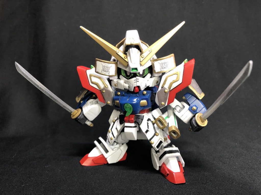 [武者閃光丸](むしゃせんこうまる)閃光丸が[暁光の鎧](ぎょうこうのよろい)を装着した姿。暁光の鎧は、閃光丸が発する光の闘気を蓄積•増幅させる効果を持つ。頬面:呼吸を制限する事を目的とした装備。鎧装着時も修行を欠かさない、という意味もあるとか。光の勾玉: 鎧胸部の宝玉。怒紋活主流を修めた証として師匠から与えられた、光の闘気を自在に操る者の証。[銘刀 明鏡•止水]父•爆流が鍛えた二本の刀。すぐにカッとなり怒りで我を忘れてしまう息子の性格を心配した爆流は、二本の刀の名を思い出す事で怒りを鎮め、何事も冷静に対処できるように願ったという。いわゆる親心ってやつですね。もともと武者のモチーフを持つシャイニングガンダムを、さらに武者寄りにするというのは思ったより難しく…(^^;;まずはLGBB体型のシャイニングを目指し、段々と武者らしくなるようにパーツを追加していきました。肩の横に足したパーツが武者っぽさを出してくれてお気に入りです。最終的には良い塩梅に落ち着けてよかったと思います。