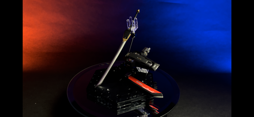 こちらはうちわのブレードを全て破壊された場合に備えての近接武器となる刀。通常時は鞘に収められているが、使用時には鞘内でブレードに充電補填された熱量を反映し、ヒートブレードして使用が可能。錫杖に比べると小回りが効くため、機動力を活かした素早い連撃も可能。ビームサーベルと比較すると、刃を熱して使用する分エネルギー量の大幅な節約となり、その分機動にエネルギーを回せるが緊急時の使用ではエネルギーの補填が充分になされていない場合、ヒートブレードとして機能しないため、鉄の装甲を纏ったMSに対しては鈍器というような使い方となる。「ちィッ!エネルギー補填が足りなかったか!?ならば叩くまで!!」