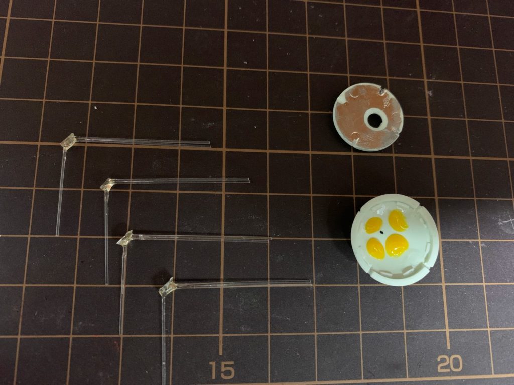 ミノフスキー粒子発生装置の上下左右4ヶ所をどう光らせるか、悩みました。使用するLEDの数はできるだけ少なくしたかったので、胴体の光をどう伝えるか、について工夫をしました。写真は最終版のものではなく、その原形です。光ファイバーを90度の角度になるようにし、小さなアルミ箔といっしょに光硬化レジンで固定しました。その後、さらにアロンアルファを周りに塗って補強してます。これで、アルミ箔に反射した光がもう一方の光ファイバーに送られています。