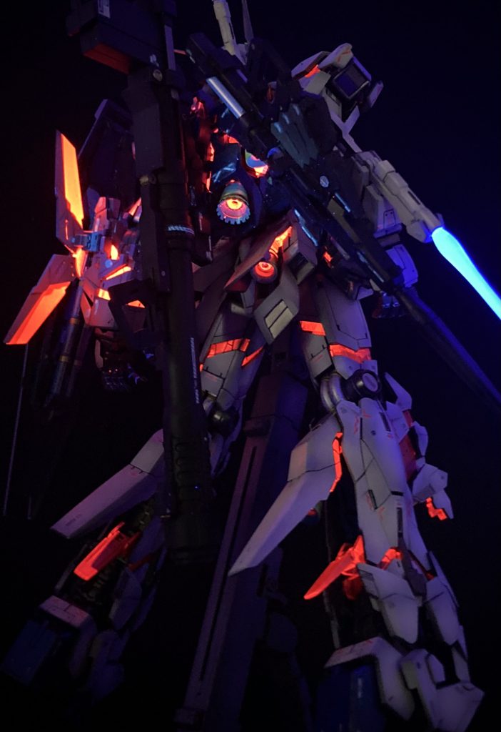 これがメインディッシュ!!デストロイモードの発光状態です。蛍光塗料のスプーキーは非常に明るく光ります。ブラックライトは推奨されている波長が365nmのものを使用しています。 サイコフレームの塗装は…プライマー(ABS素材なので)→黒サフ(もともとのクリアパーツのピンク色の発光を抑える)→クレオススーパーゴールド2で立ち上げ→クレオスGXメタリックルージュ→クレオスGXクリアルージュ→スプーキーレッド(蛍光塗料)→クリアというように塗り重ねました。メタリックの上に直接スプーキーを吹くと金属粒子がうきあがることがあるのか、発光がまだらになることがあったので、クリア層を間に入れることでこれを防いでいます。ビームサーベルもスプーキーブルーで発光させています。