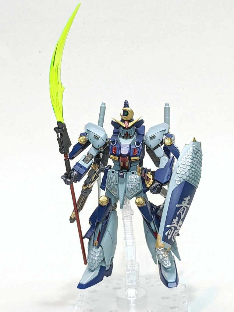 意匠としてSD版を参考にし、Z系の機体であることから武者精太(ゼータ)を強く意識。他に武者摩亜屈(Mk-Ⅱ)等、他の武者、それ以外でフルアーマーZ、なども参考。頭はSD版の鳥帽子型兜、全体を当世具足(とうせいぐそく)でイメージ。また設定に「青龍」のワードが出てくるので、龍を意識しつつ製作を行いました。・鳥帽子兜(とりぼうしかぶと)まず立物(たてもの)ですが頭部の特徴的なアンテナをなくし、開き気味のV字アンテナに変更。これを前立(まえだて)、鍬形(くわがた)としました。兜はHGUCドムトローペンに旧キットサザビーの顔先でモノアイ部分を生かし成形。これをかぶせました。兜の前立はZガンダムのアンテナでなく、SD版の印象を生かした月形状を取付。この前立てはSD烈破頑駄無。V字アンテナはビルダーズパーツHD使用。・胴巻(どうまき)胸部腹部装甲に当たりますが追加の増加装甲にしようかとも思いましたがディティール追加でとどめました。・脇楯(わいだて)腰部のサイドアーマーになりますが左右グレネードラックを外し、ジーエンアルトロンの装甲に変更。武器の取付ができるように加工。・臑当(すねあて)脚部の鱗装甲以外に、膝の辺りもジャンク部品のHGUC百式,Mk-Ⅱの脚部を増加装甲にしました。