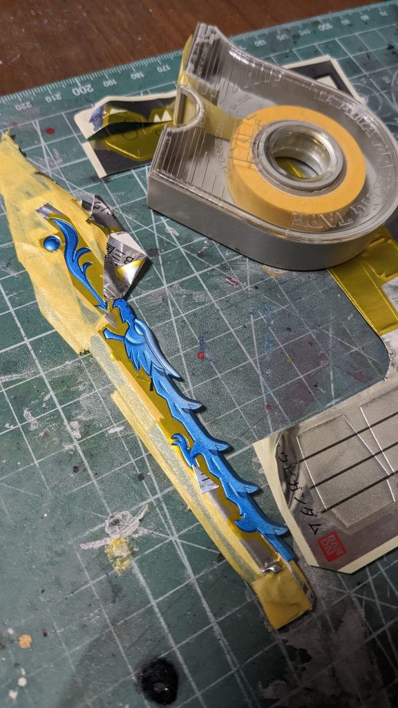 このキットで一番手間がかかったのがこの剣。竜の模様は金色になるのですが、先にメタリックブルーを塗装してしまったのでシールの余白部分を貼ってマスキング代わりにしてます。やってる途中で気づいちゃった！金色を塗装してから竜の模様にシールを貼ればもっと楽にマスキング出来ましたよねって・・・