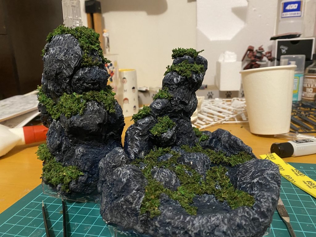 青っぽい黒を下地に塗って、黒で影になりそうなところ塗って、全体的にグレーでドライブラシして、岩の光の当たりそうなところに白でドライブラシしてみましたー!そして、仕上げに100円ショップのコケみたいなやつを刻んでボンドで固定したら完成〜!でも和風っぽいね…馬鹿にされた!