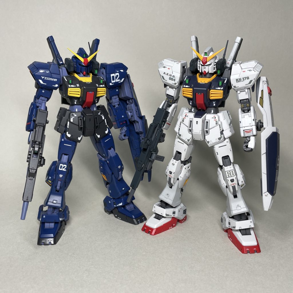RGマークⅡ エゥーゴカラーと並べて まえ エゥーゴカラー(白)は、外装部分をランナーについたままエアブラシ塗装、スミ入れしました。その後、適度に組み立ててから細部を筆で塗り分けています。 塗った色のせいもあってか、撮影途中からRGの白マーク2の足が陸戦ガンダムの足のように思えてきました。平均的なガンダムの足のデザインに寄ってしまった印象を受け、細部ディティールがきっちりしているのは素晴らしいのですが、マーク2のアニメ設定画のスネの部分のデザインの魅力が削がれてしまった気がします。(あくまで私個人の意見です。気を悪くされたらすみません。)