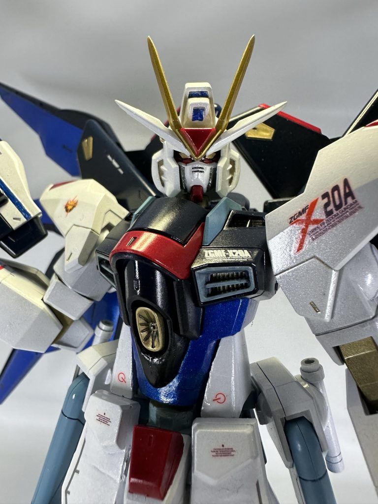 顔についてですが「馬面、大きい、縦に長い」などとよく言われるので、マスク(への字のある白いパーツ部)の下を1~1.5mmほど削って縦長だったのを短く。赤い顎パーツも前を1~1.5mmほどカットし、下も削って小型化しました。額の赤いパーツも左右合わせて1mm少々削っています。そしてヘルメット両サイドのダクト部も外側にパテを少し盛ってマスクに幅をもたせて縦長に少しでも見えないようにしました。またボディは下部を延長しています。