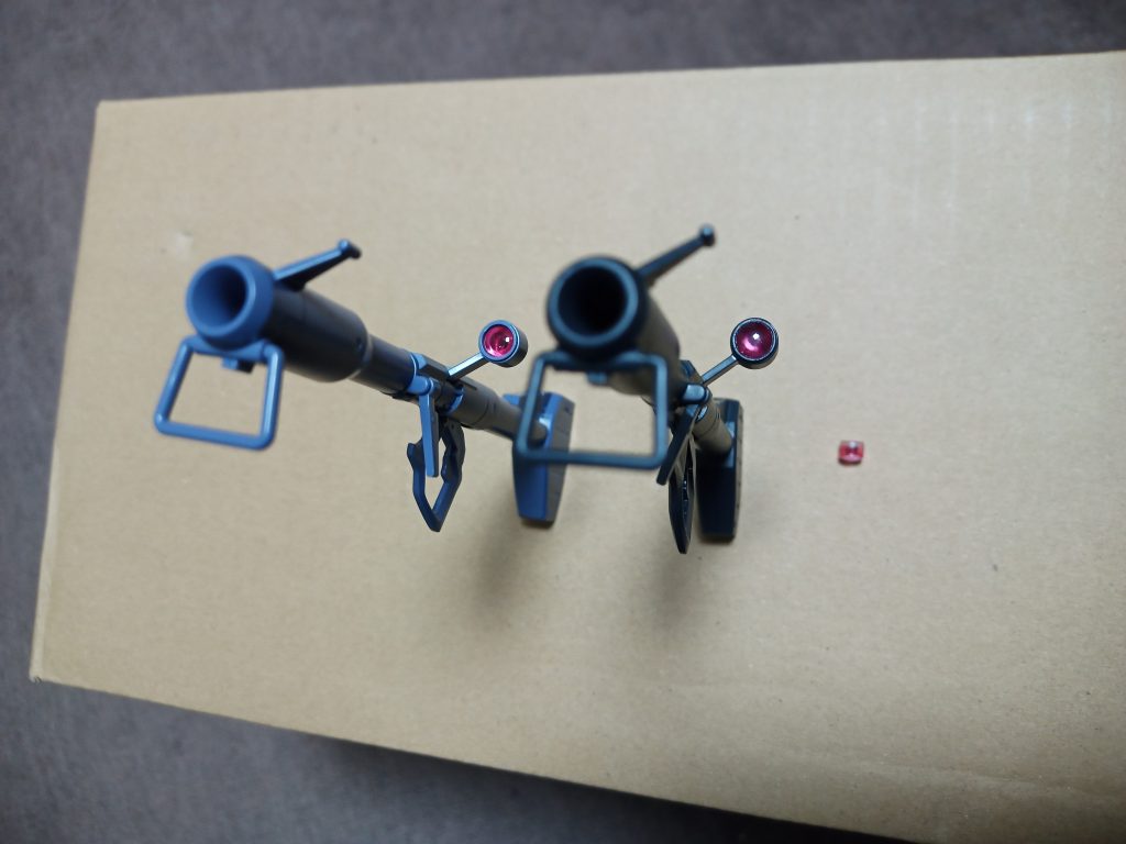 ジャイアントバズを組んだ際に「ハメ殺しのスコープの中に細かいランナー破片が混入」というとんでもないミスをしてしまいエグる→レンズパーツがダメになる→Hアイズに変更→仕様が変わったので純正品が欲しくなりジャンク入手→結局スコープ内部はシルバーに塗りたいのでジャンクのレンズパーツも外したい…を経てエグるとまたダメになるのでレンズ中央にランナー切れ端を瞬接で接着してツマミとし、周りの隙間にはグリスをしみ込ませて地道に引っ張って何とか外れた状態の物を再GETできました(左が磨き終わった純正、右がHアイズ、その右に転がってるのがダメになったクリアパーツです)Hアイズにした方はジャーマングレーで塗って以前作ったグフ飛行試験型の専属武器へと転用する事にしました^^;