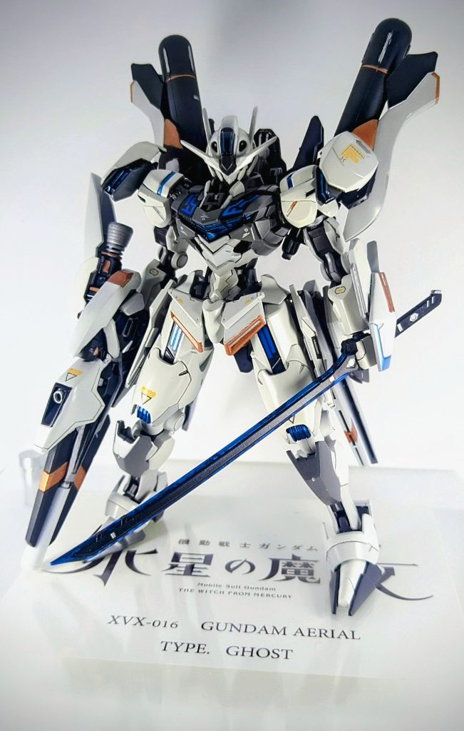 フロント画像になります。エアリアル本体には、両肩のアーマーに切り飛ばしたバックパックのブースターを増設、膝にクアンタのアーマーを移植しました。シルエットとして、素のエアリアルよりマッシブになるように意識し、バックパックと腰部に増設したマルチユニットによってX型のシルエットに整えました。カラーに関しては、水星の魔女の作中における実戦使用のMSは皆、モノトーンなカラーをしていたのでそれに習い、明るめのカラーはあえて避けて作成しました。しかし、あまりにもモノトーンでは作成自体の映えが無くなってしまうと感じたので、カッパーやデカールをオレンジにすることで少しアクセントを加えています。