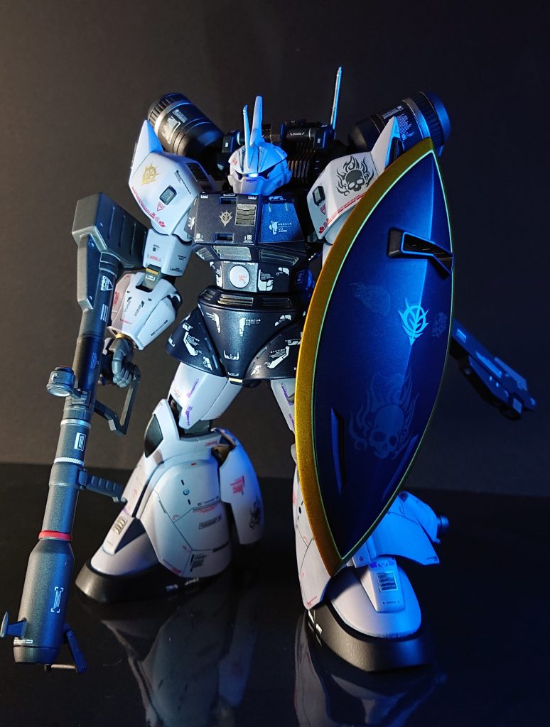 全身ショットです。今回カスタムするにあたって以下のような妄想設定のもと作成しました。自己満レベルの内容で恐縮ですが晒しておきます。。＝＝＝＝＝＝＝1年戦争末期、量産体制に入る前のゲルググが一部の部隊に配備されていたが、統合整備計画本格実施前段階にも関わらず、既にゲルググＪやMに近しい高機動型カスタム機が存在していたという設定。※ただし当時の技術力では高機動型バックパックを小型化する事はできず、プロペラントタンク含め、かなり大きいものとなっており、更に排熱処理が課題であったため至る所に排熱用のダクトなどが設けられていた。パイロットは大柄なポリネシアン系のベテランエースパイロットで全身にタトゥーが入っている。その機体は自身同様、胴体周りを中心にトライバルタトゥーを模したようなマーキングを施した機体となっている。武装についてはこのベテランパイロットがビーム兵器にはまだあまり信頼をおいていないため、ジャイアントバズや両刃タイプのヒートソードなどの実弾/実物兵装を優先して使用する傾向があった。1年戦争末期から終戦後の連邦軍によるジオン残党狩りにおいて、対峙した際、大ぶりのヒートソードを振り回し相手を圧倒するほどの活躍を見せるが、デラーズフリートやシーマ達に合流することもなく、自身のテリトリーを犯す輩をただひたすらに殲滅することに終始していた模様。なお、連邦軍からは、蒼白く光るひとつ目（モノアイ）、高速移動で瞬時に現れ離脱する様、両刃タイプのヒートソードの形状、更にはジオン残党狩りにおいて、戦場で対峙した部隊がほぼ全滅しており、帰還した者が少なく具体的な目撃情報もごくわずかであった事から ”Ghost of the halberd” の異名で恐れられたという。。＝＝＝＝＝＝＝