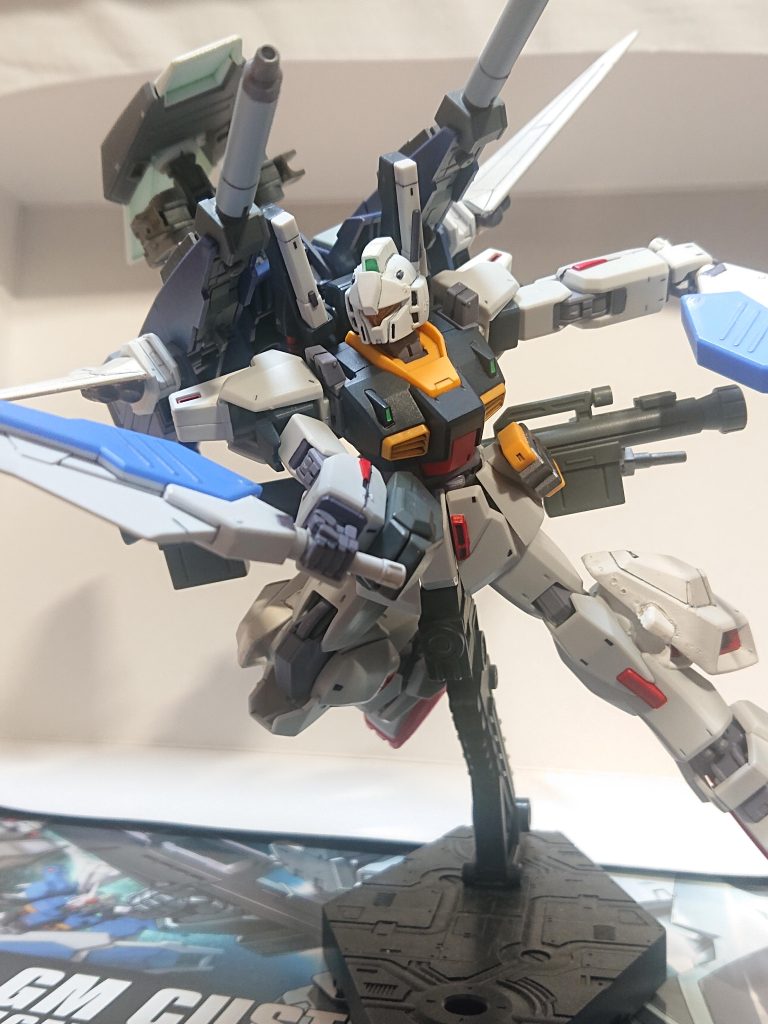 解説文④:本機の運用本機はUC0097年、夏野エミ中尉の誕生日である4月15日に受け渡され、同日の慣熟飛行にてバウを指揮官機とする袖付き残党の可変MS部隊による襲撃を受けた。結果として単機にてMS5機を撃墜、さらに母艦も見つけそれも大破、拿捕する事に成功した。また、ゼータタイプとの交戦もあったとされるがその詳細は分からない。機体についても、難なく乗りこなしており多機能を活かすだけでなく、MVSのビーム・ガンも格闘戦の最中に織り混ぜて相手に防御を強制させるなど牽制以外にも活用するなど、改造を行った側の想定外の戦術も駆使した。彼女以外のパイロット用にも本オプションは数基製作されたが、乗りこなせるパイロットは限られているため実質彼女の専用装備だった。上の写真は撮影時期は不明、一説によれば先述のゼータタイプとの戦闘であるとの事だ。解説文⑤へ続く