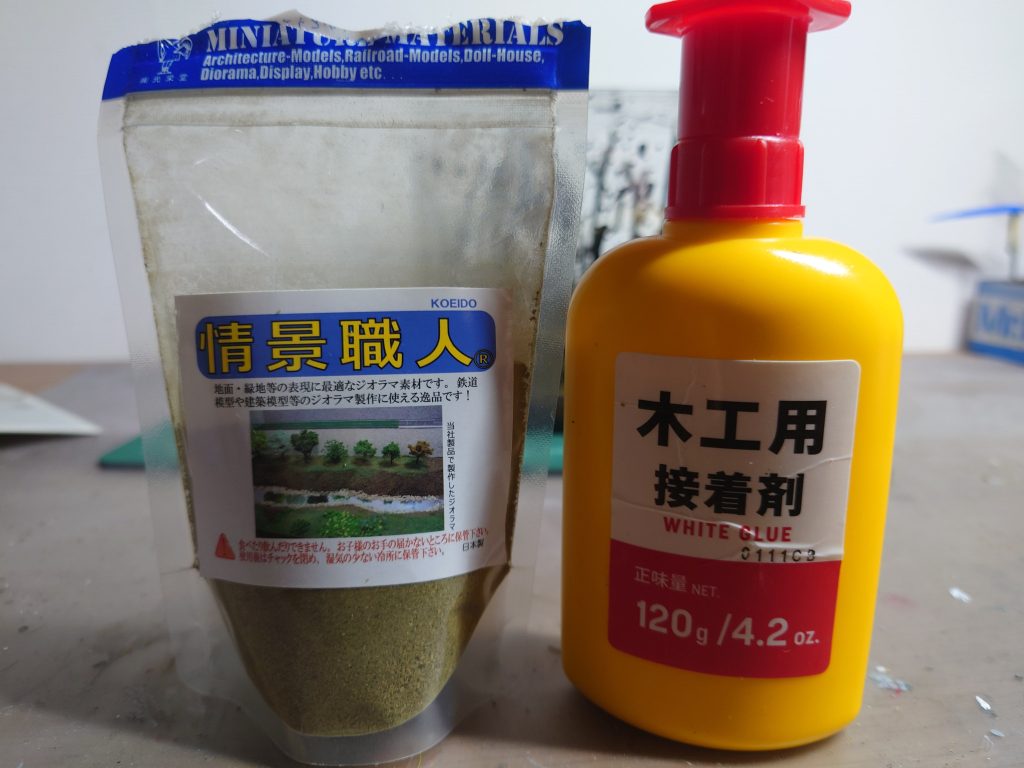 地面や機体、建物にはジオラマで使われる情景職人の青のりみたいな素材を使いました。振りかける前に木工用水性接着剤を水で溶かした物を作り、草を乗せたいところに溶かした物を筆で塗り、その上に青のりをかけて制作しました。