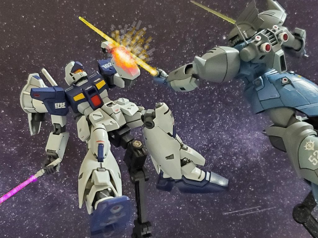 傷ついたジムカスタムに最後の一撃とばかりにビームサーベルを振るゲルググM❕しかし、シールドを破壊されたジムカスタムは、回避するのではなく、破損覚悟でビーム刃を左腕で受け止める😵💦