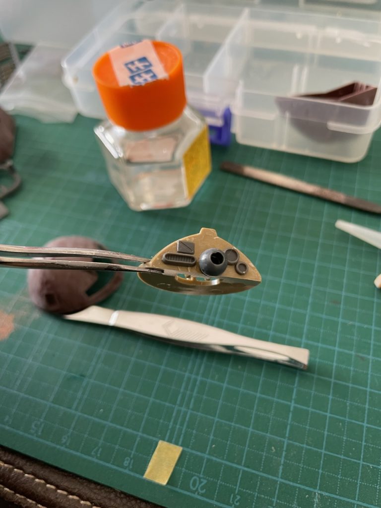 モノアイシールを貼り付ける曲面をカットして現れた垂直面に色々貼り付けました。中央に余剰パーツのPCキャップ配置し、5mmのキラキラストーンをモノアイに見立てて貼り付け。余白に、コトブキヤの丸モールド、ハッチ、排気ダクト等をテキトーに配置。