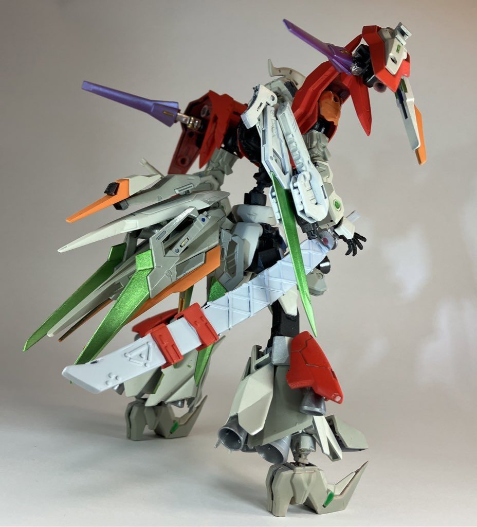 ガンダムフレームをベースに腰を細く縦長の独特のデザインを意識して作りました。多様な戦闘シーンに備えるために武装は多く、多機能な物を装備させました。太刀はロマンです(笑)頭部はプラ材等で耳を作り、顎を延長して、胸部はパテで盛り独自のデザインを作りました。左腕にはデスティニーの肩をベースにビームサーベル搭載の多機能シールド、右肩にはMGブルーDの装備を移植しました。カラーリングはクリーム色と赤をベースにしつつ差し色でオレンジやグリーンを使いました。グリーンがかなり差し色として効いていて個人的には満足です！まさに漢の背中、ですね、！！脚部にバーニアを盛り強い推進力をイメージさせました。またクアンタのパーツをベースにビットとドラグーンを集約させる「オールレンジリアベース」を装備させました。