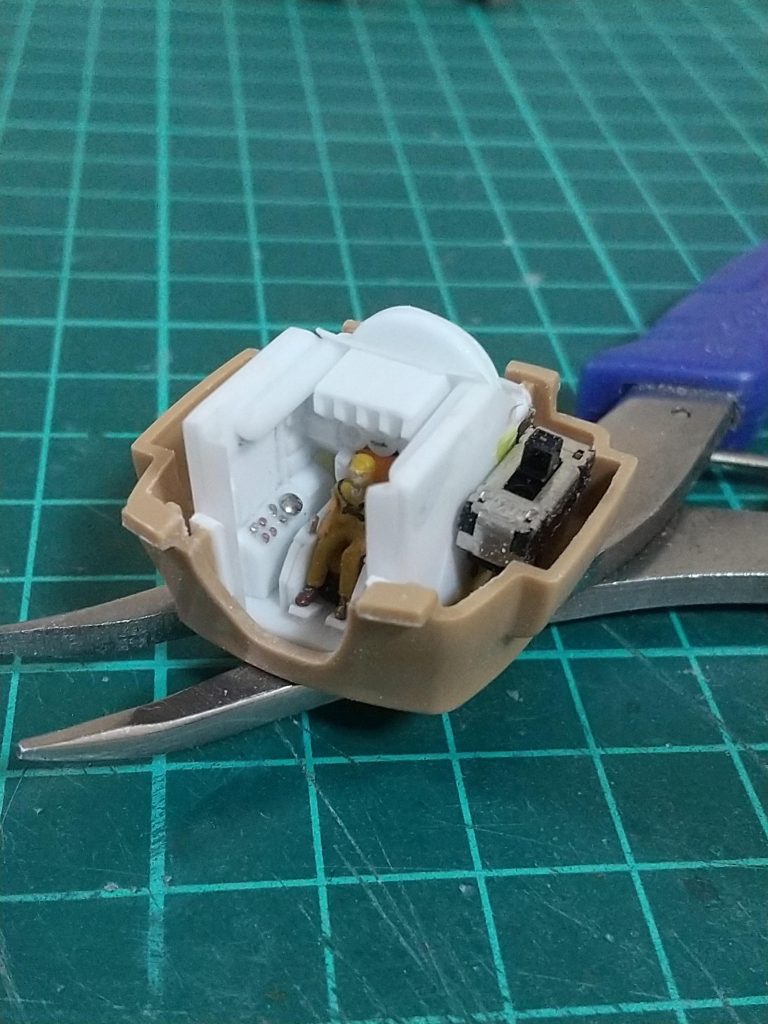 コックピットは自作です。1/144サイズなので今の私の腕ではこのあたりが限界ですが、キンバライド基地所属の兵士っぽく仕上げたパイロットを乗せています。コックピットの後ろ側に電池を、横側に電飾のスイッチを配置しています。