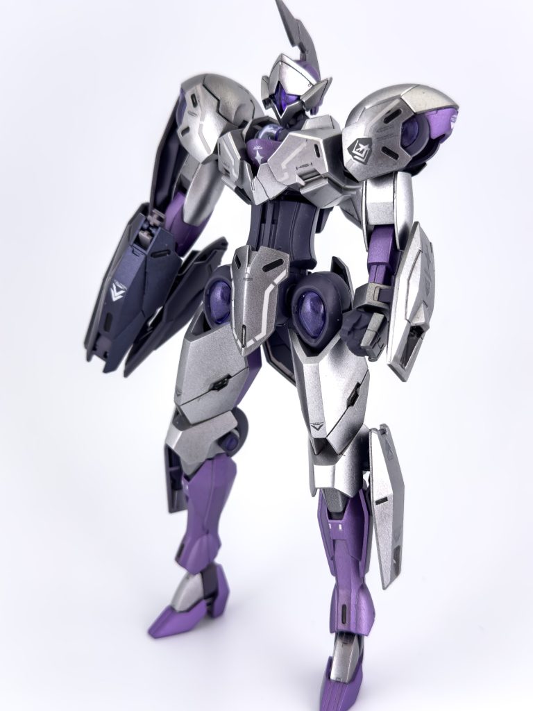 大きな改修はありませんが、膝アーマー横がさみしく感じたのでレンズパーツをつけてみました。ビルダーズパーツのMSサイトレンズを塗装したものを使用しています。また、首も1mm延長しています。今回はシルバーの塗装にこだわってみました。効果のほどはさておき、3層塗りで仕上げています。下地は黒サフで1段目はクレオスダイヤモンドシルバー+GXクリアシルバー、2段目はガイアEXシルバー+クレオスGXメタルバイオレット(3%程度)、3段目はガイアスターブライトシルバー+GXメタルバイオレット(1%程度)という具合にしています。また、最後のコートはガイアEXクリアーとガイアEXセミグロスクリアープレミアムを独自混合したものを使用し金属感を損なわずに滑らかな表面になるような仕上げにしています。