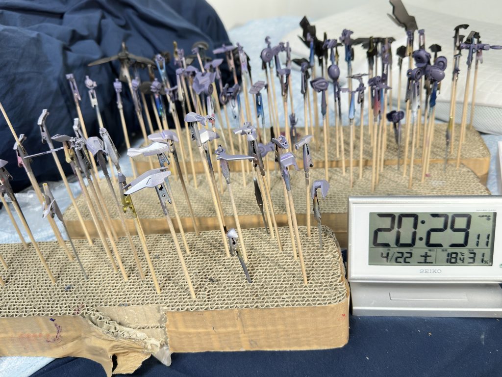いつもはパーツ洗浄するのですが乾燥時間がもったいないので、アルコールシートで脱脂してハンドピース最大エアーで残ったチリややすりの粉を塗装ブースに吸わせて飛ばします。今回かなりうまくいったのでもうこれでいいかもしれません。そして、画像はサフ終わりの時間で20:29。棒付けが18:50くらいに終わった気がするので1時間半ほどでサフ工程は終わっています。フレームはここで終了になるので、シルバー外装(黒)→パープル外装(シルバー)→フレーム(パープルグレー)の順に塗装して乾燥時間を稼ぎます。部屋で除湿器動かしてプロユースシンナー使っているのでぬって数分後にはほ乾燥しているのですが念のためです。部屋のスペースの問題で布団の上に置いていますがご了承ください。