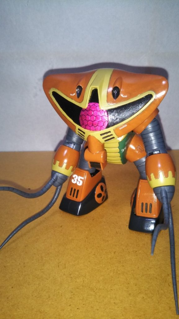 正面素立ちです。 使用したキットは旧キットの1/144アッグガイです。 キットの箱絵に描かれている一般的な配色ではなく、ZZガンダムに登場するカラーリングをイメージして塗装してみました。 この「ZZ版」アッグガイ、初めて見たときにはあまりにも悪趣味に感じたのですが「少し色味を調整してやれば、意外とリアルな感じに仕上がるんじゃないか・・・?」と思い、挑戦してみました。 基本塗装は、頭部などがレッドブラウンにミドルストーンなどを混ぜた茶色、胴体が緑にニュートラルグレーを混ぜた少し明るめのグリーン、胴体の蛇腹(?)などがミドルストーン、手足の蛇腹部分やヒートロッドなどがニュートラルグレーにツヤ消し黒を混ぜたいつもの暗いグレーです。 足首がミッドナイトブルー、口(?)のインテーク部分などは黒鉄色です。 また、モノアイはシルバーで下地を塗装し、スミ入れペンで複眼のスミ入れを行ったあと、マッキーのピンクで塗装しました。 ZZ版の設定イラストで黄色だった部分をミドルストーンにしてやるだけで、想像以上にミリタリーチックなカラーリングになりました。 太ももの蛇腹や腕部などはかなり加工を加え、ポージングや立ち姿が極力野暮ったくならないように工夫しました。 また、このキットの弱点として「頭部が上向き過ぎる」という点がよく指摘されるようなのですが、こちらの写真のようにやや前傾姿勢にすればそれほど違和感はないように個人的には感じたので、頭部の位置は全くの無加工です。