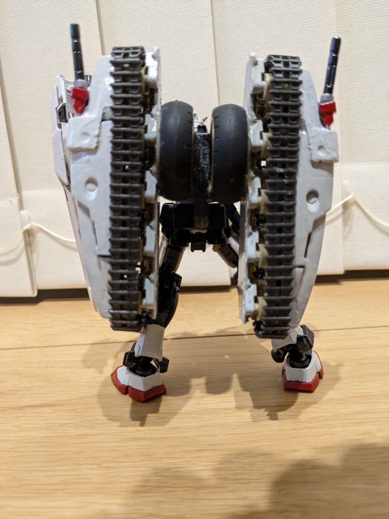 バックショット。腰リアアーマーにコマンドガンダムの余剰パーツを利用して作った追加バックパックを設置。そこから両サイドに、家に眠っていたミニ四駆のタイヤ、そして作成途中で眠っていた戦車のキャタピラ、最後に旧1/100トールギス3のバックパックを半分ずつ装着し、ビームサーベルのラックを接着しました。かなりリアヘビーになりましたが、意外と自立できました（笑）