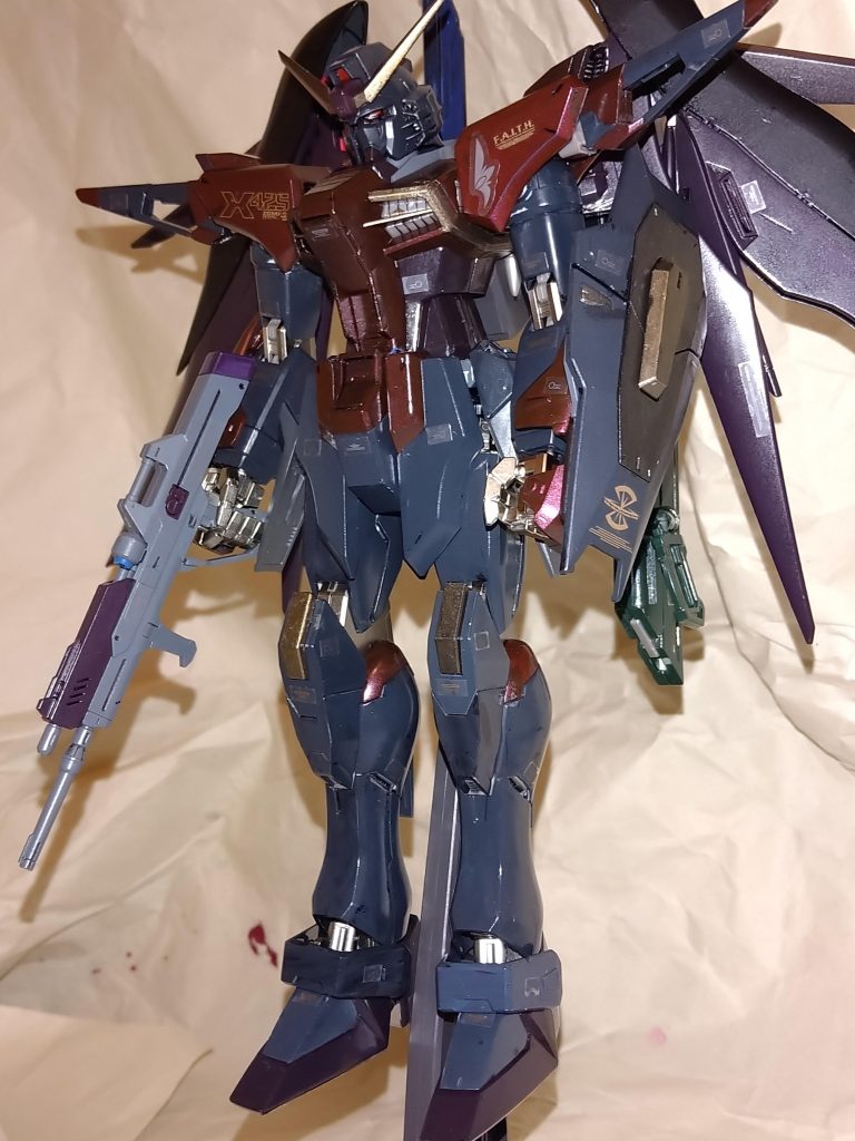 悪役面と呼ばれた顔が更に悪役面になりましたw使用した塗料はアクリジョンの光沢のレッド、ブルー、グリーン、ブラック、ゴールド、グレーバイオレット。半光沢のメタルブラックを使用しました。一番苦労したのは上半身の色合いです。カラーイメージは仮面ライダー響鬼のマジョーラカラーをイメージしてレッド、ブラック、ゴールドを混ぜ合わせてましたが、仕事終わりの合間で塗装してたので色合いに差が…………。腰部とバックパックと脚、ビームライフルの一部にはレッドとブルーと少量のブラックを混ぜ合わせてみました。次に全体とシールドの色にはグレーバイオレットとブラックを混ぜ合わせて更に暗い色合いにして、頭部のアンテナとシールドと膝にはブラックとゴールドを混ぜ鈍い金色にしました。