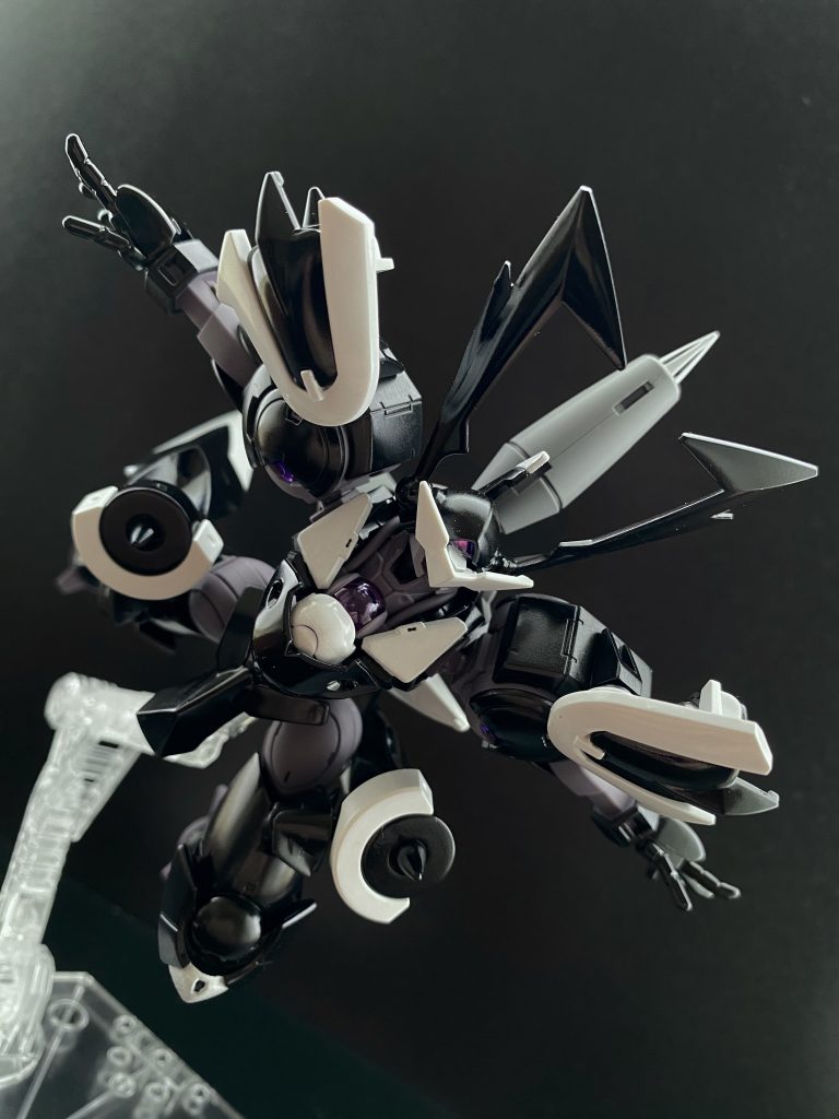 　決闘が始まってすぐ、スレッタは自分の目を疑うことになる。目の前のモニター、画面に表示される相手の機体情報、そして、距離。距離500。「え…」　決闘が始まった際、互いのコンテナは、1500ほどの距離があったはず、そんなに広いフィールドではない、しかし平坦でもない。障害物も多い。にも関わらず、「は、速くないですか…」　狼狽するスレッタ、しかしそこは、ホルダー、そしてエアリアルである。瞬時にエスカッシャン、ガンビットを展開する。それと同時に、モニターに映るこちらに真っ直ぐ、地面すれすれを飛ぶように突っ込んで来る黒いハインドリーを捉える。　黒いハインドリー、自ら「スサノオウ」と名付けた機体のコクピットの中、モニターに捉えたエアリアルを見据え、グラハムは言い放つ。「抱きしめたいなッ！ガンダムッ!!」　両手を広げ、真っ直ぐ突っ込んで来る黒いハインドリーに困惑しながらも、正確にその機体の各部をロックオンしていく、ガンビットは既に相手の左右、そして後方に展開している。後は減速の瞬間に斉射すれば良い。　しかし、そのタイミングが訪れたスレッタに待っていたのは、この決闘が始まって二度目の驚嘆。躱されたのだ。前後左右、ほぼ全方位からの攻撃を。黒いハインドリーは、縦軸を中心にくるりと機体を回転させ躱わすと、そのまま、タックルするようにエアリアルにぶつかって来る。　その様子を中継で観ていたチュチュが叫ぶ。「ウソだろっ、背中に目ぇついてんのかよっ！」　そんなチュチュの声はコクピットにいるグラハムには聞こえない。しかし当のグラハムは、まるでチュチュと会話しているかのように叫び返す。「心眼は鍛えているッ！」　エアリアルの上に馬乗りになった黒いハインドリーは、その手でエアリアルの頭部をガシと掴み上げると、コクピットのグラハムは薄く笑みをたたえ言う。「…まるで、眠り姫だな」