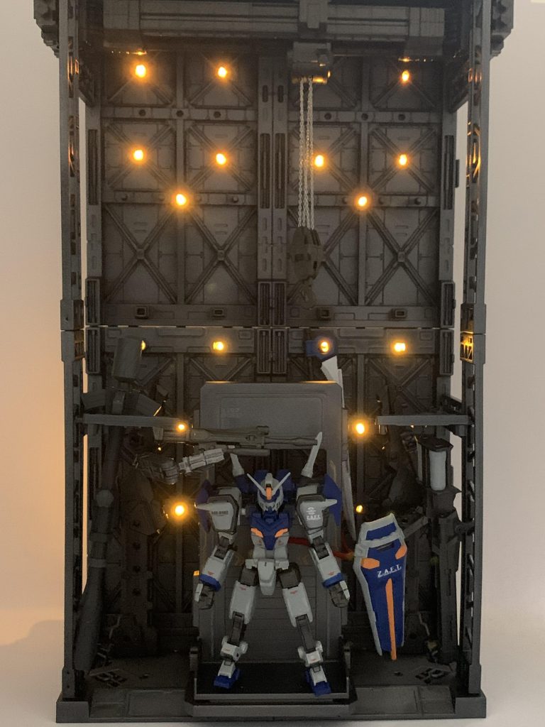 今回は何故か基地まで作ってしまった。みんな御用達山田化学さんの100均連結ディスプレイベースを基にチェーンベースやホワイトベースMSハンガー、エヴァフレームの輸送台、30MMのカスタマイズトラスベース、コトブキヤヘキサギアのクレーンオプションを組み合わせ100均ジュエリーライトで電飾も追加。ワニスチューブやリード線も組み合わせアースリィのリアアーマー接続を貼り付けケーブルに本体を繋ぎ充電？してる風にも出来ます。