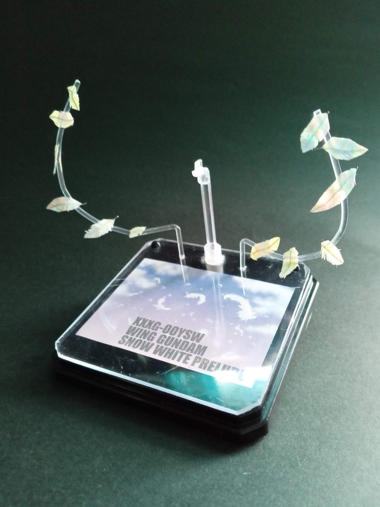 エフェクト台座。100均のフィギュア用ケースの台座に100均のフォトプレートを切って上底部2か所で止めてます(ぬいぐるみの目を使用:手芸店で購入)プラ棒で羽の軸を作り羽貼って、フォトフレームに入っていた支柱とアンサンブルの台座の接続部分だけをくっつけて台座に接着。フリー素材の羽の情景に機体番号入れたものを印刷して挟んで完成💦