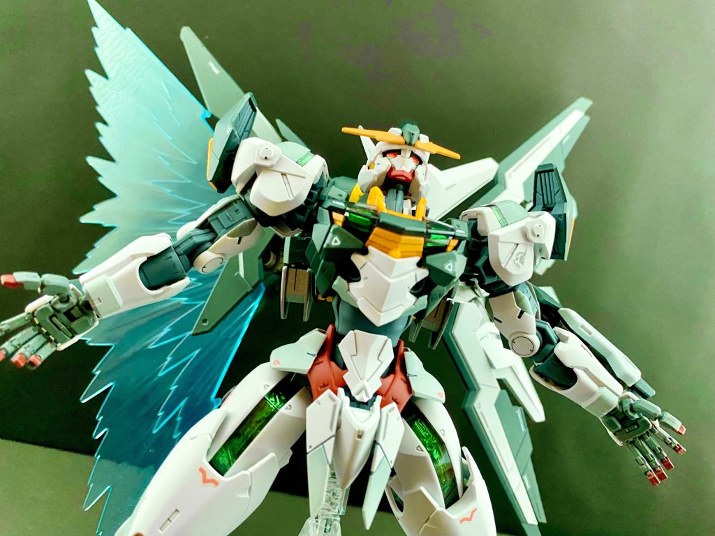 金色のダリルバルデのコクピットの中、グエルは見た。エアリアルのシェルユニットが今までに見たことのない輝きを放ったのだ。〜♫ア〜ア〜ア〜ア〜、アアアアア〜♪〜(ユニコーンガンダムのあの曲)グエル「…なにが起きてる」 強い緑色の光を放つシェルユニットの輝きは、やがて機体全体から放たれる。それと同時に、今までセンサーユニットだと思っていたパーツが展開。そこから溢れ出たパーメットの粒子が光の翼を形成したのだ。 その翼は瞬く間に巨大な帯状に形を変えて、ダリルバルデを含めた周囲のMSを、クワイエット・ゼロの外壁から文字通り引き剥がしていく。そして、クワイエット・ゼロ全体を包み込むように拡がると、その光の色を濃い虹色に変えていく。エアリアルと共に虹色の光に包まれるシャディクが言う。シャディク「これは、パーメットの共振?人の意思が集中しすぎて、オーバーロードしているのか?なのに、恐怖は感じない。むしろ暖かくて安心を感じる」シャディク「しかし、この暖かさを持った人間が、地球さえ破壊するんだ」 そんなシャディクの中に、心に、緑色の光が、スレッタの思念が流れ込んでくる。「わかっています。だから、世界に、人の心の光を見せなきゃならないんです」 そうしたシャディクの目には、エアリアルのシェルユニットの中心とした各部から、まるで溢れるように虹色の結晶が、エアリアルを覆っていくのが見える。 グエルは、今、目の前で起きている事が信じられずにいた。虹色の光の中、クワイエット・ゼロの落下スピードが、目に見えて落ちていく。人型の結晶体になったエアリアルが、巨大なクワイエット・ゼロを止めたのだ。エアリアルが光の翼を出してから、何度もスレッタを呼んでいる。しかし、何度呼んでも返事はない。そんなグエルに、接触通信により、思いがけない声がかかる。「おい、グエル!聞こえてんのか、おい!」グエル「お、お前…、無事だったのか…」 チュチュである。見ると、半壊したバオリパックから、ワイヤーが伸びて…。チュチュ「あぁ、こんなこともあろうかと、デミの方じゃなくて、バオリパックの方から操縦してたんだよ」 あの時、爆散したのはMS本体の方だったのだ。安堵するグエルにチュチュは言う。チュチュ「おいグエル、男と見込んだ。スレッタとミオリネを頼む」 そうだ。まだあそこには、スレッタと、ミオリネがいる。グエル「ふ、コロシ文句だな…」 グエルは、金色のダリルバルデのスロットルを踏み込み、もの言わぬ、スレッタの元に向かう。